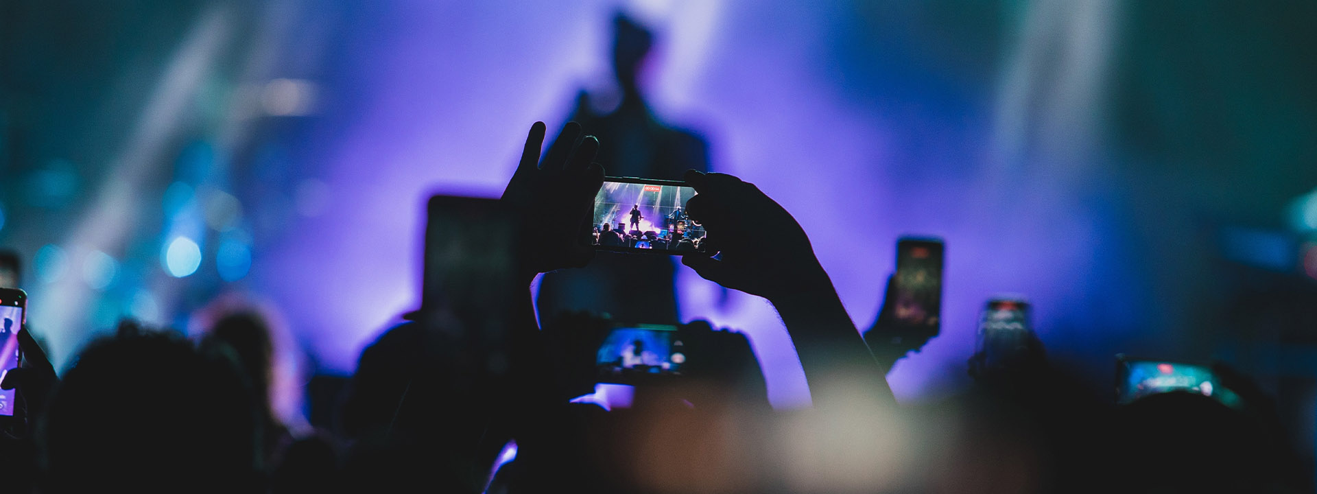 A person holding a cell phone with a band performing on stage