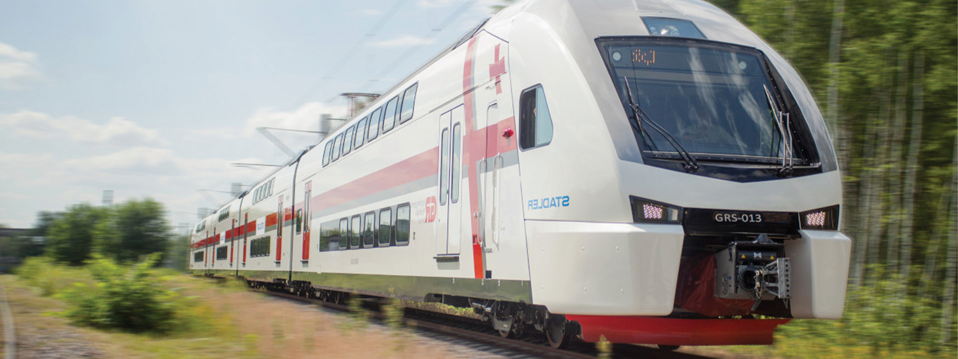 A sleek, modern double-decker passenger train with white and red stripes travels on a track through a scenic area with trees and clear skies.